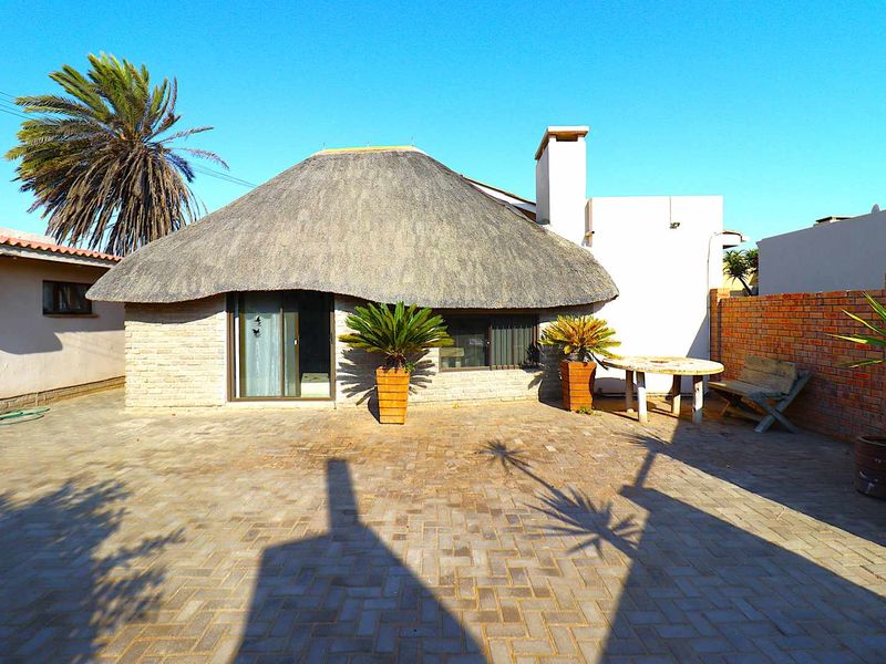 Rear exterior view of a house featuring a traditional thatch roof, paved courtyard area, and brick boundary wall.
