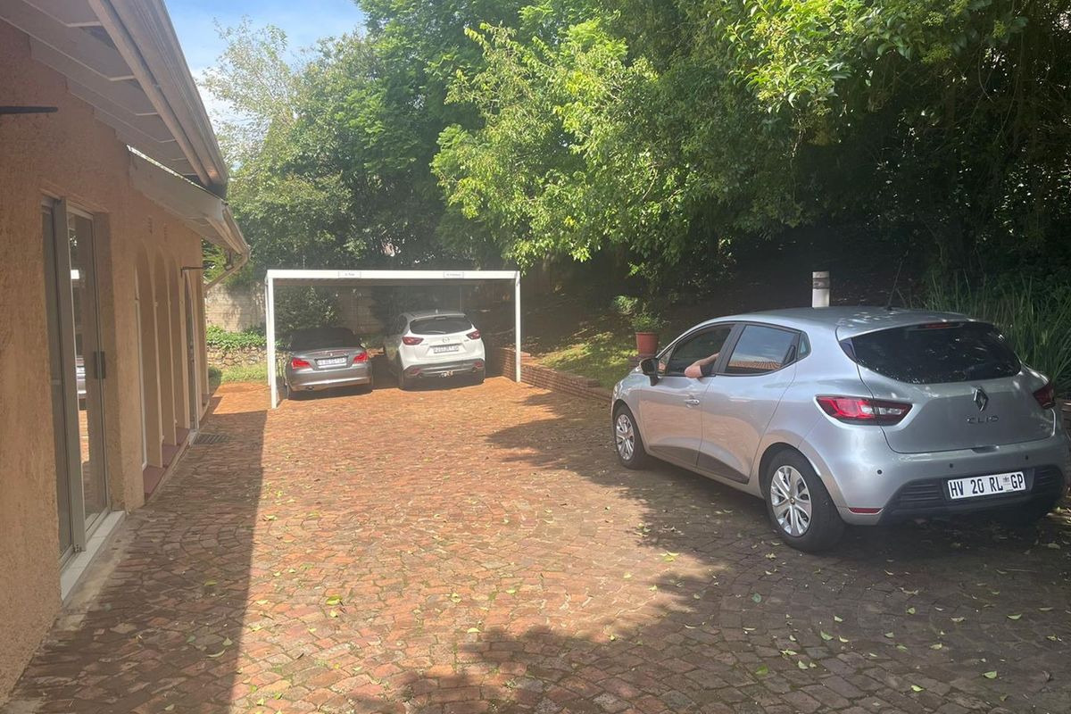 Exterior view of the property featuring a paved driveway, covered carport structure, and mature surrounding trees.