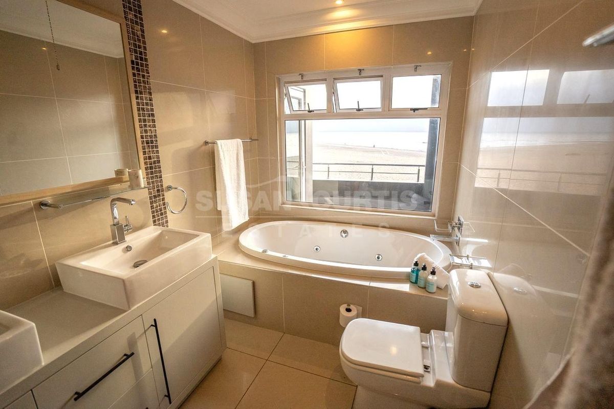Modern bathroom featuring a built-in bathtub, vanity with basin, and tiled finishes, offering a bright space with a view.