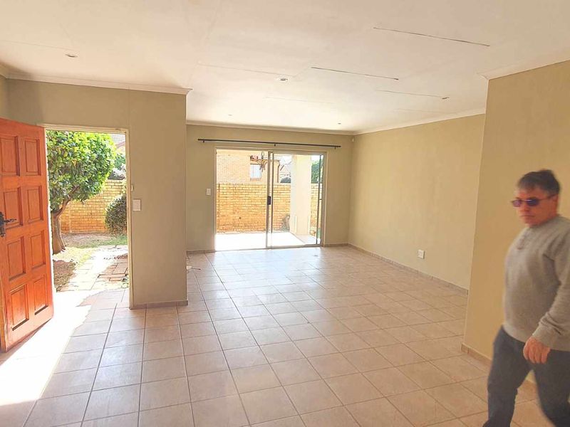 Spacious, empty living area featuring tiled flooring, a wooden entrance door, and sliding glass doors leading to the exterior garden space.