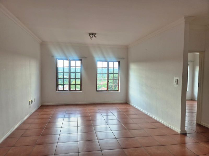 A spacious, empty living area featuring tiled flooring, classic wooden frame windows, and neutral walls, offering a bright and versatile space.