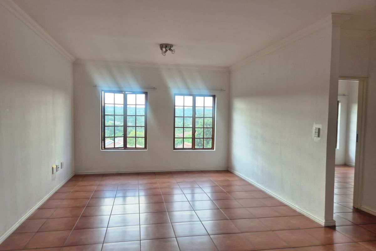A spacious, empty living area featuring tiled flooring, classic wooden frame windows, and neutral walls, offering a bright and versatile space.
