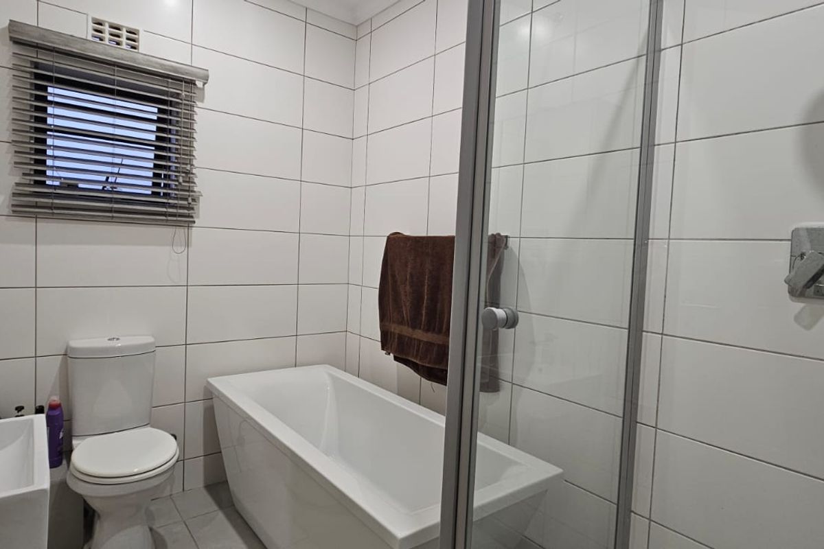 A modern bathroom featuring white wall tiles, a bathtub, a separate shower enclosure, a toilet, and a basin with a mixer tap.