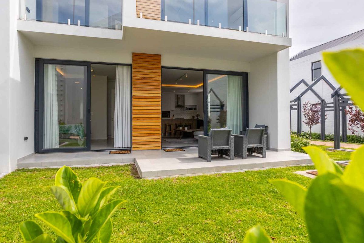 A modern rear exterior view featuring a tiled patio, timber-clad accents, and large sliding glass doors leading into the open-plan living area.