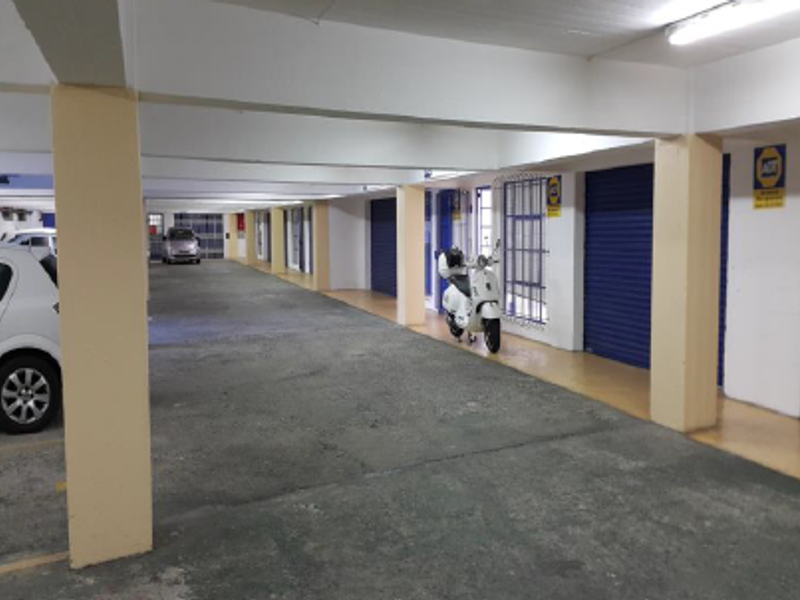 A spacious covered parking garage featuring concrete columns, roller shutter doors, and functional overhead lighting.