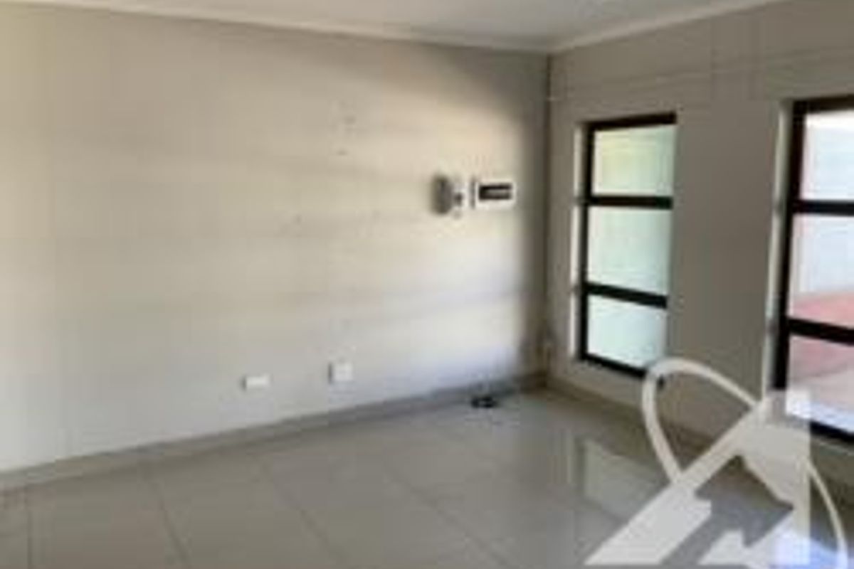 An empty, tiled living room featuring neutral walls, aluminium-framed windows, and recessed lighting, offering a clean canvas for interior design.