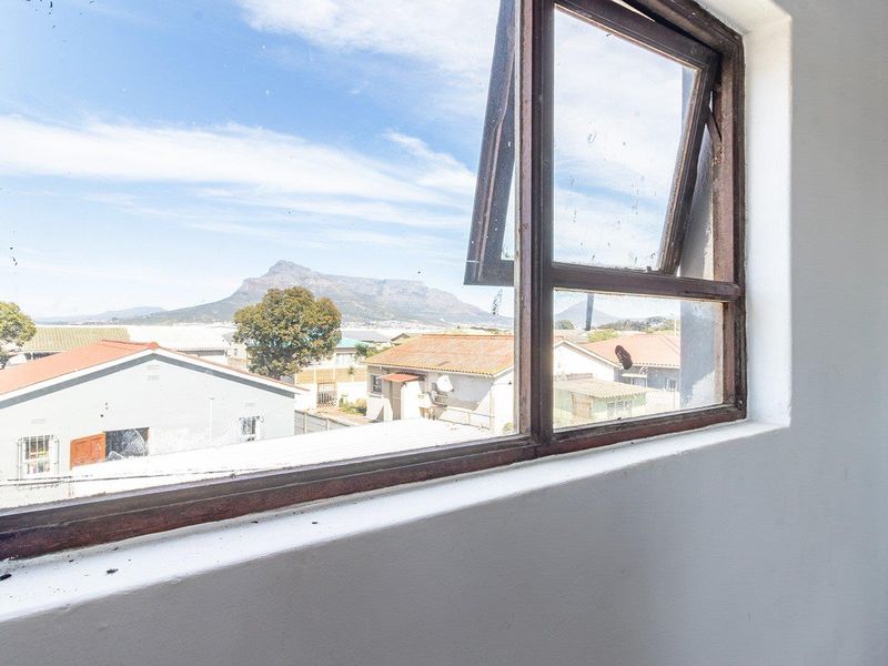 A view from an interior room looking out through a timber-framed window towards a mountain landscape and surrounding residential area.