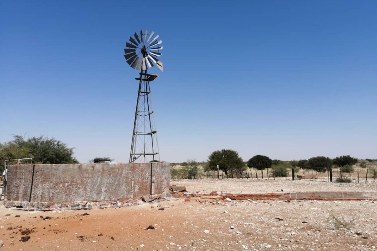 A rural farm scene featuring a traditional metal windmill and a circular concrete water reservoir set in an open landscape.