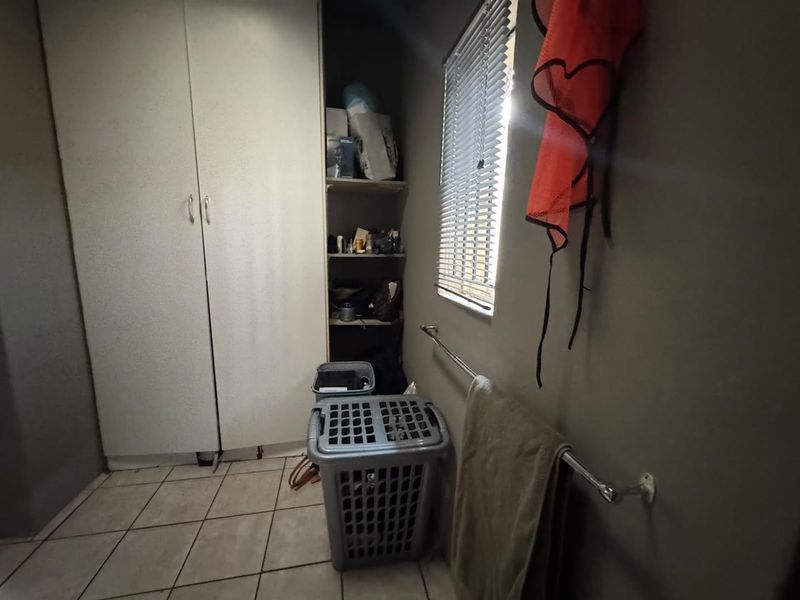 A functional laundry area featuring built-in storage cabinetry, tiled flooring, and a window with venetian blinds.
