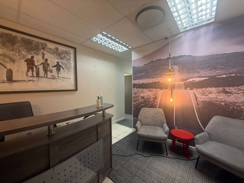A professional office reception area featuring a built-in reception desk, carpeted flooring, drop ceiling with integrated lighting, and a decorative feature wall.