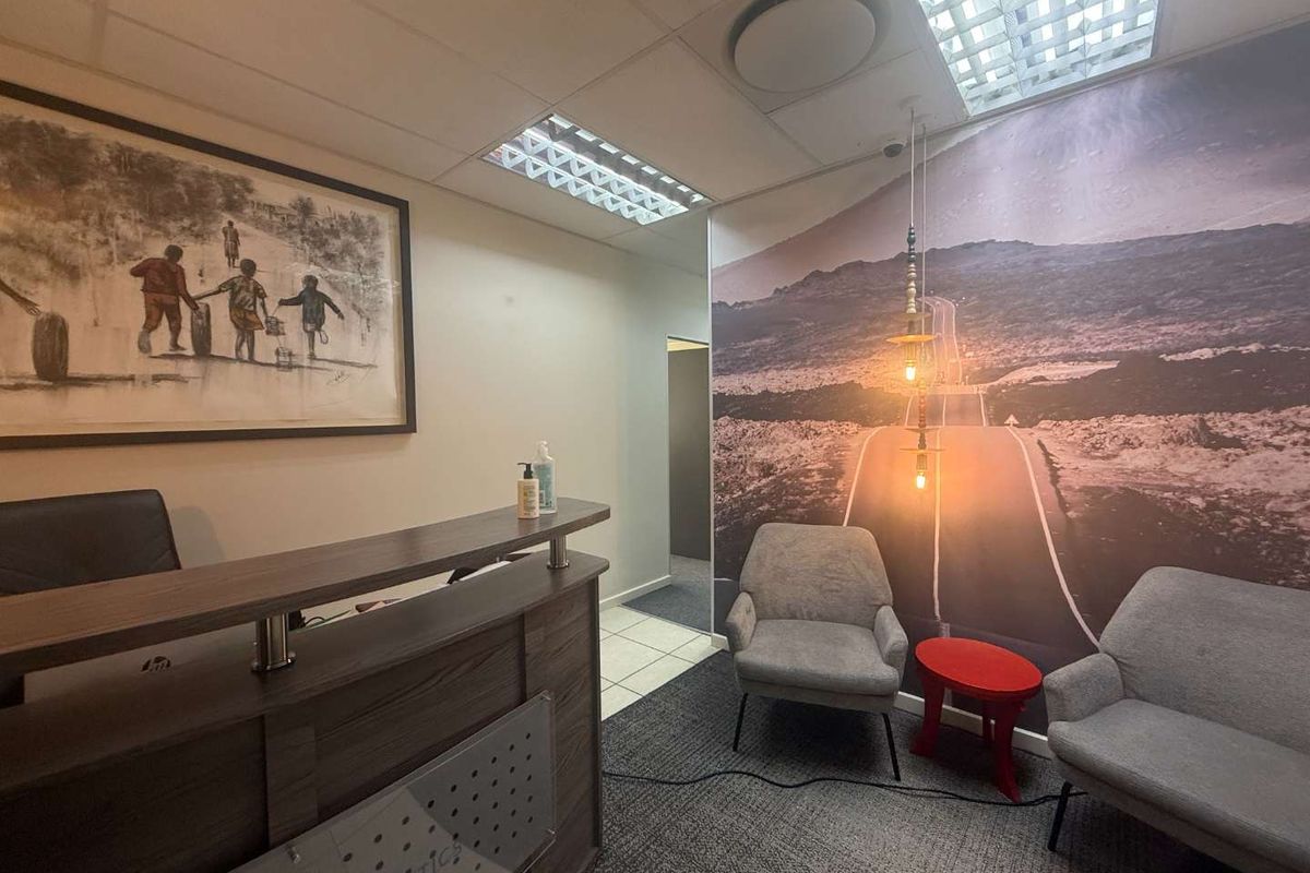 A professional office reception area featuring a built-in reception desk, carpeted flooring, drop ceiling with integrated lighting, and a decorative feature wall.