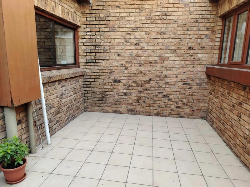 A private, paved patio area featuring face brick walls and aluminium window frames, offering a blank canvas for outdoor living and entertainment.