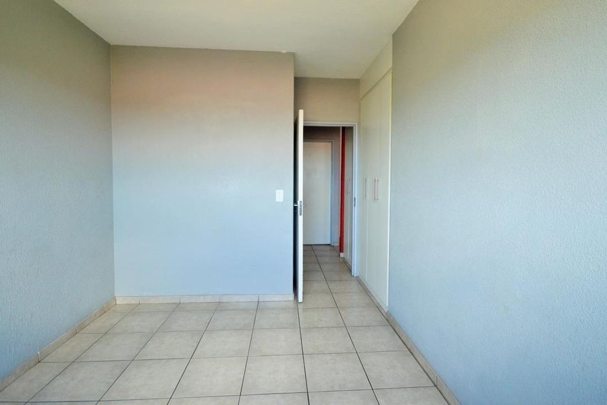 An empty bedroom featuring neutral-toned walls, tiled flooring, and built-in cupboards, providing a clean and versatile space.