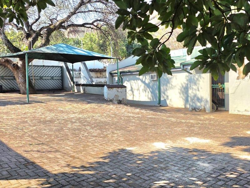 Rear exterior area featuring a paved surface, shade sail structure, and perimeter wall with security fencing.