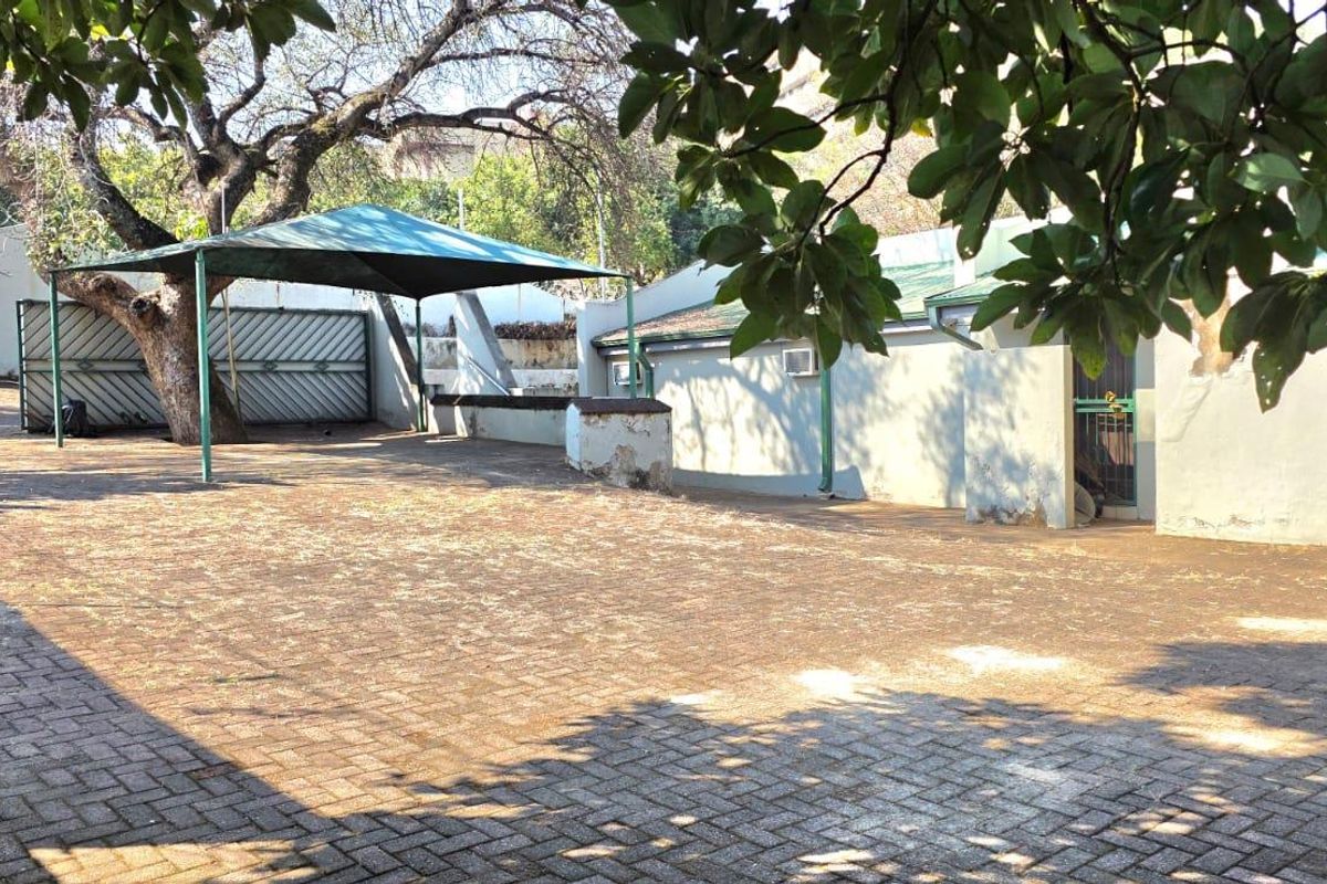 Rear exterior area featuring a paved surface, shade sail structure, and perimeter wall with security fencing.