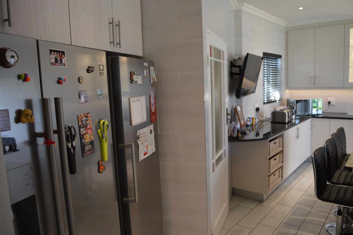 Modern kitchen featuring light-toned cabinetry, dark granite countertops, tiled flooring, and integrated storage solutions, creating a functional and well-lit culinary space.