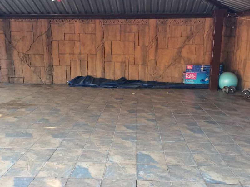 A covered outdoor patio area featuring tiled flooring and a textured stone-effect feature wall under a corrugated metal roof.