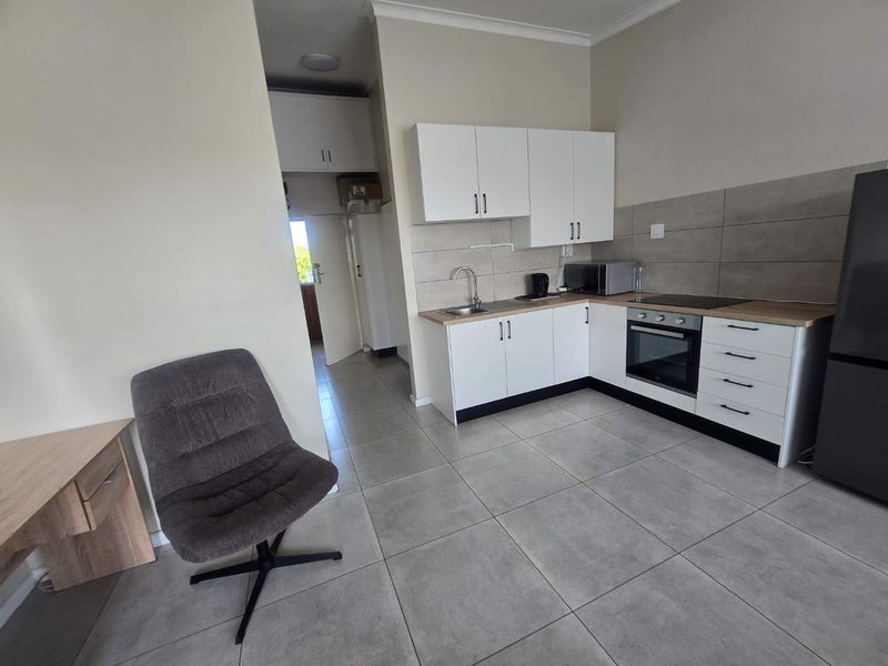 Open plan kitchen area featuring modern white cabinetry, tiled flooring, built-in oven, and hob, seamlessly integrated into the living space.