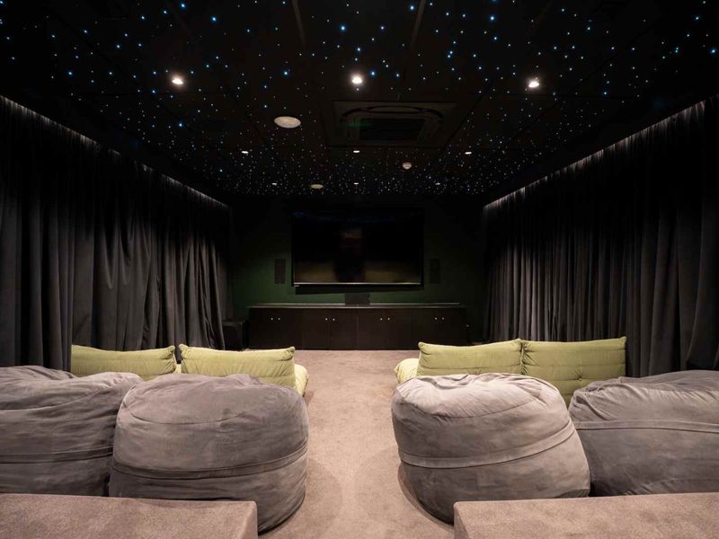 A dedicated cinema room featuring a star-field ceiling, integrated air conditioning, built-in cabinetry, and plush wall-to-wall carpeting for an immersive viewing experience.