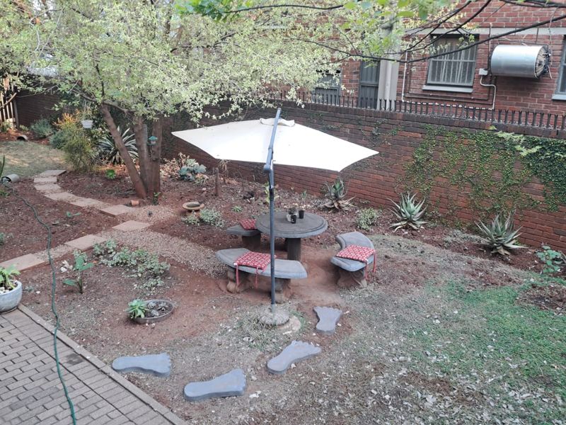 A private garden area featuring a brick boundary wall, paved walkway, and established trees, providing a quiet outdoor space.