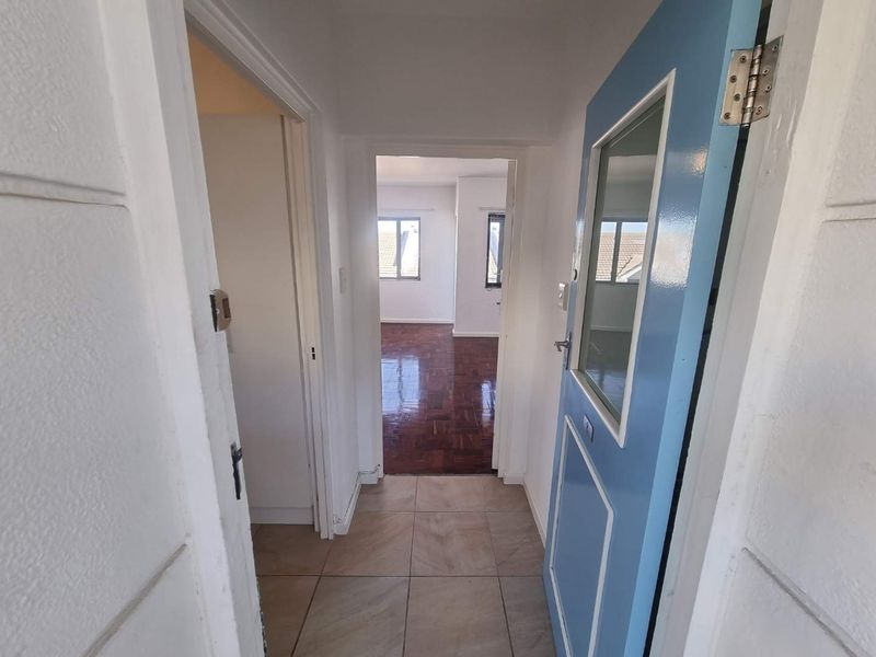 An entry hallway featuring tiled flooring leading into a living area with polished parquet floors and natural light.