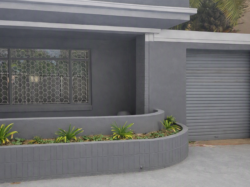Front facade featuring a roller shutter garage door, security window grilles, and a curved masonry planter box.