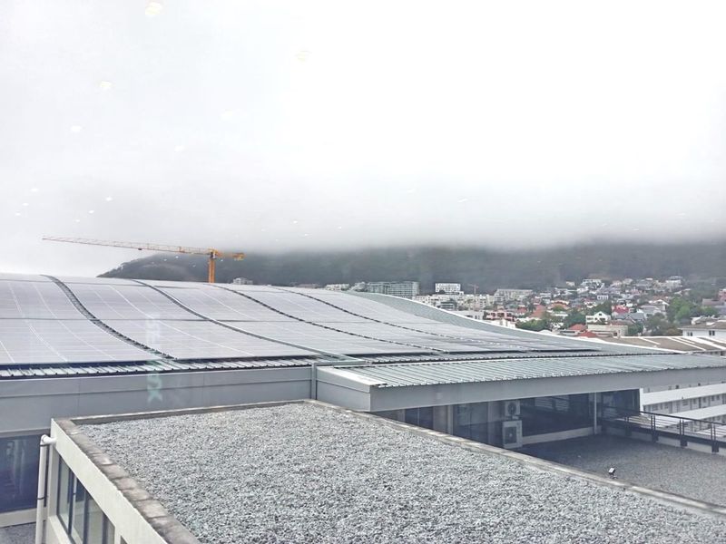 Elevated view overlooking a large commercial building roof equipped with extensive solar panel arrays, set against a mountain backdrop.