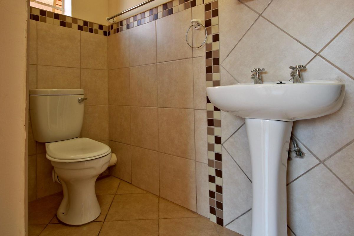 A functional bathroom featuring a pedestal washbasin, ceramic toilet, and neutral tiled walls with decorative mosaic accents.