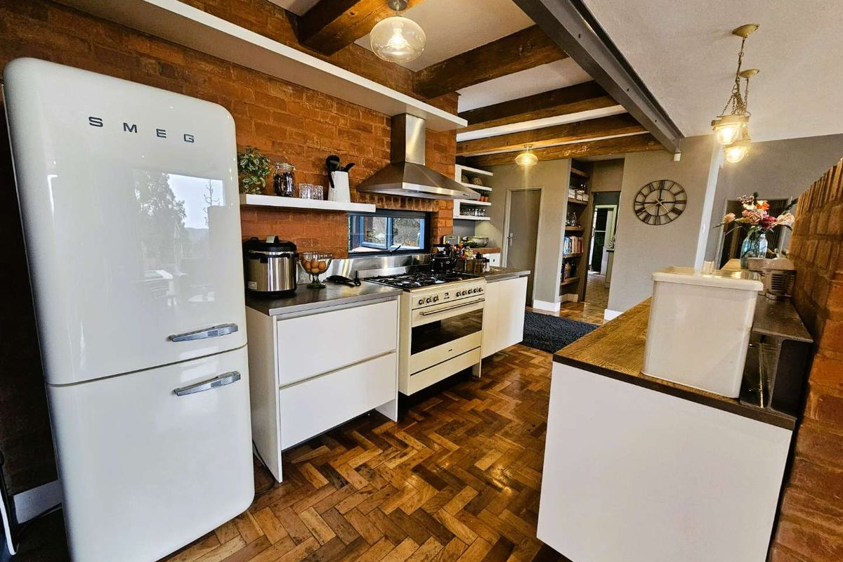 A rustic-style kitchen featuring exposed brick walls, timber ceiling beams, herringbone wood flooring, and modern white cabinetry with a stainless steel range and extractor.