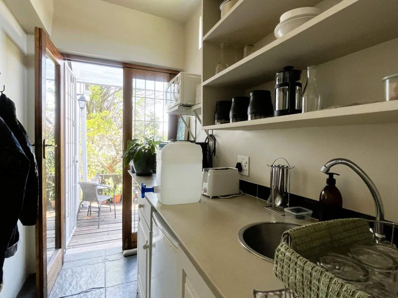 A functional scullery area featuring built-in shelving, a sink, and direct access to an outdoor patio through a glass panel door.
