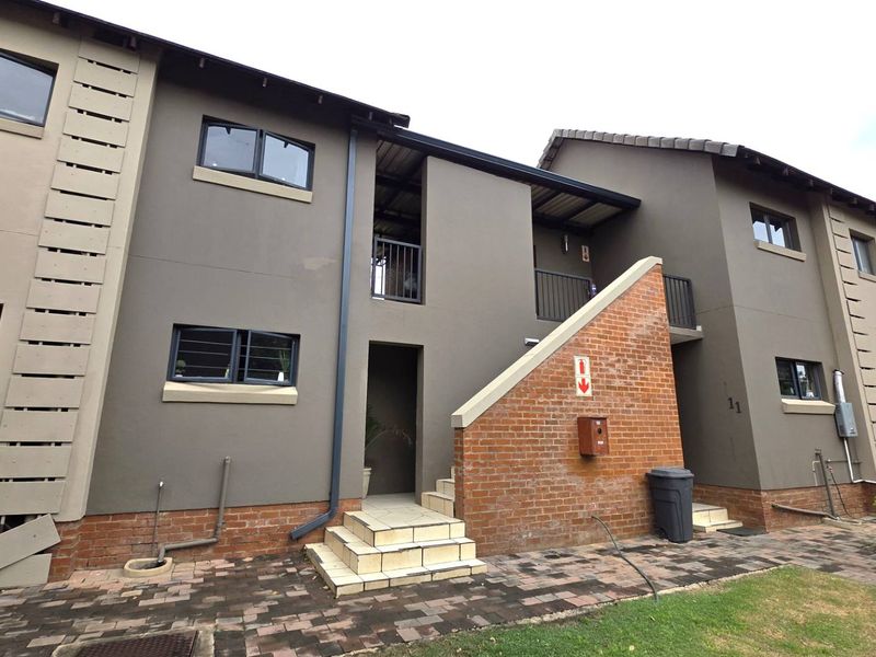 Exterior view of a multi-story apartment building featuring a brick and rendered facade, tiled staircase, and paved ground level access.