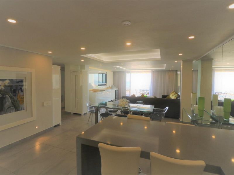 Spacious open-plan living and dining area featuring modern recessed lighting, a central kitchen island, and sleek tiled flooring with seamless flow to the balcony.