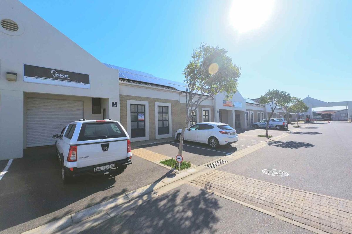 Front elevation of an industrial unit featuring a roller shutter door, brick facade, and roof-mounted solar panels with dedicated parking.