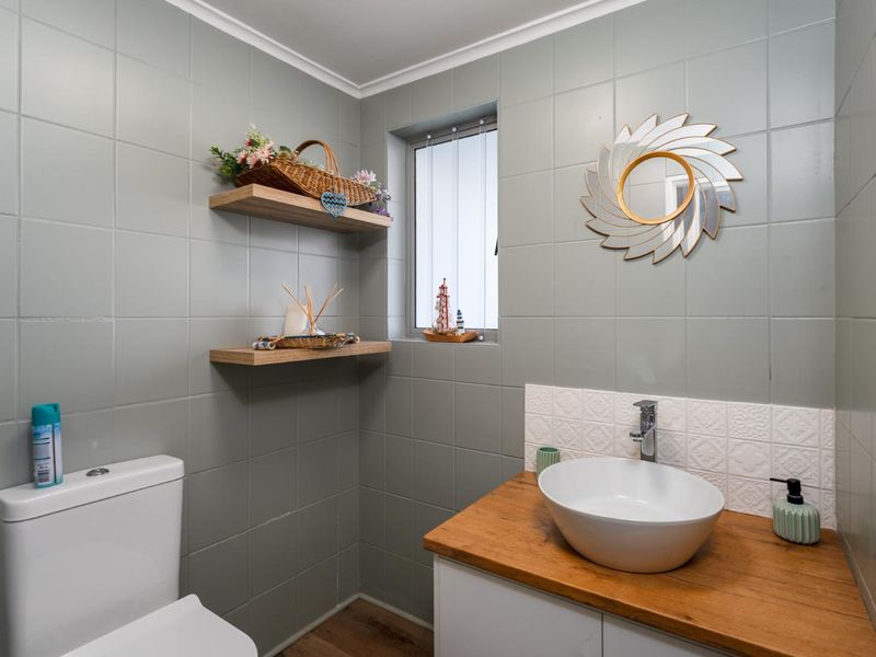 A modern bathroom featuring grey wall tiles, a vessel sink on a wooden vanity, and floating shelves.