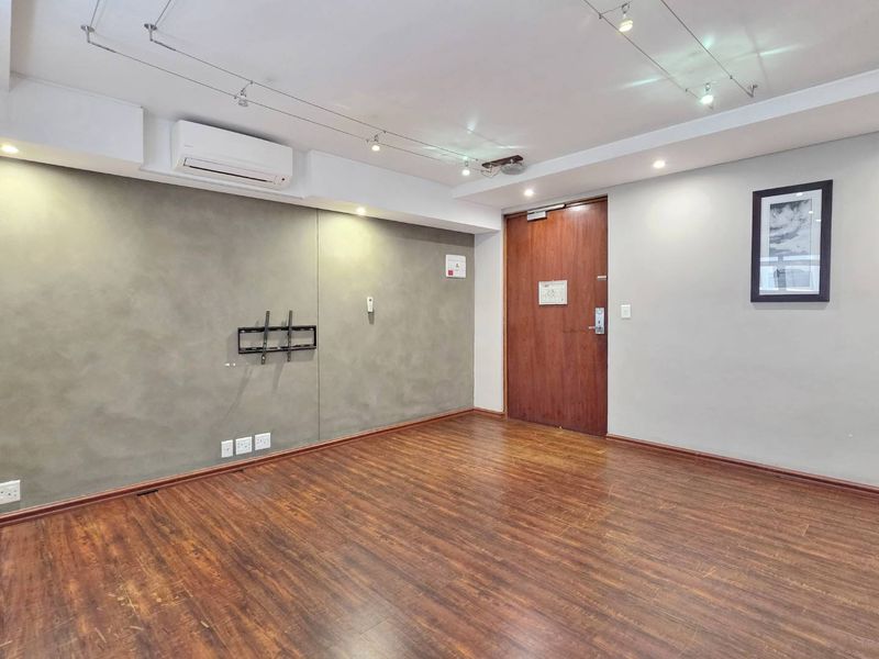 An empty living room featuring laminate wood flooring, track lighting, and a wall-mounted air conditioning unit.