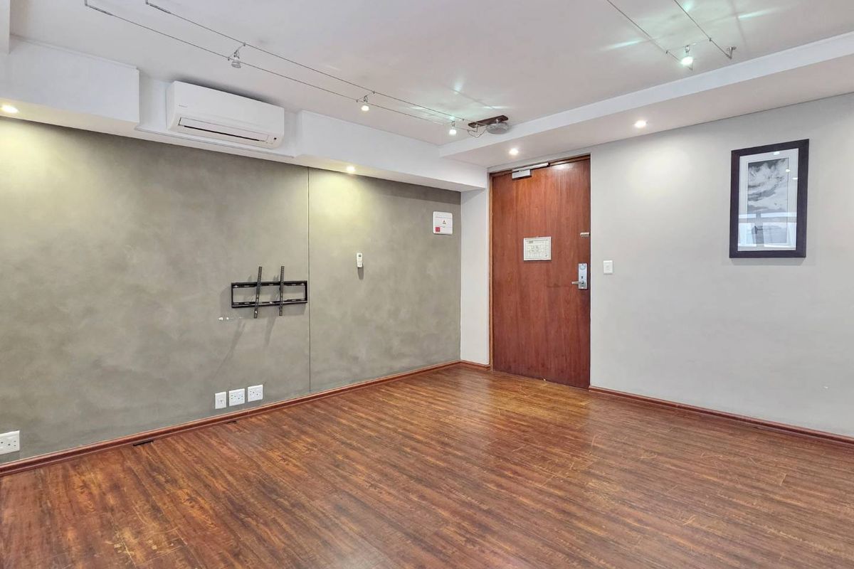 An empty living room featuring laminate wood flooring, track lighting, and a wall-mounted air conditioning unit.