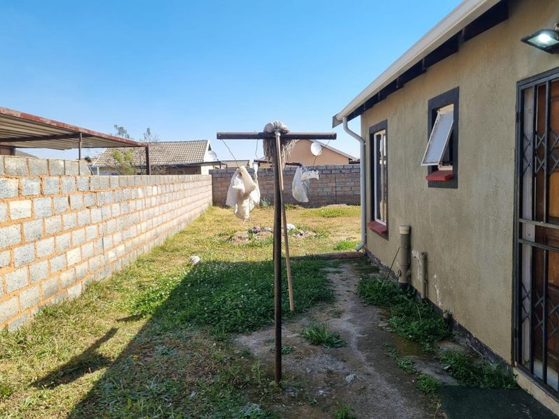 Rear exterior view of the property featuring a concrete block boundary wall, security gate, and basic garden area with a concrete pathway.