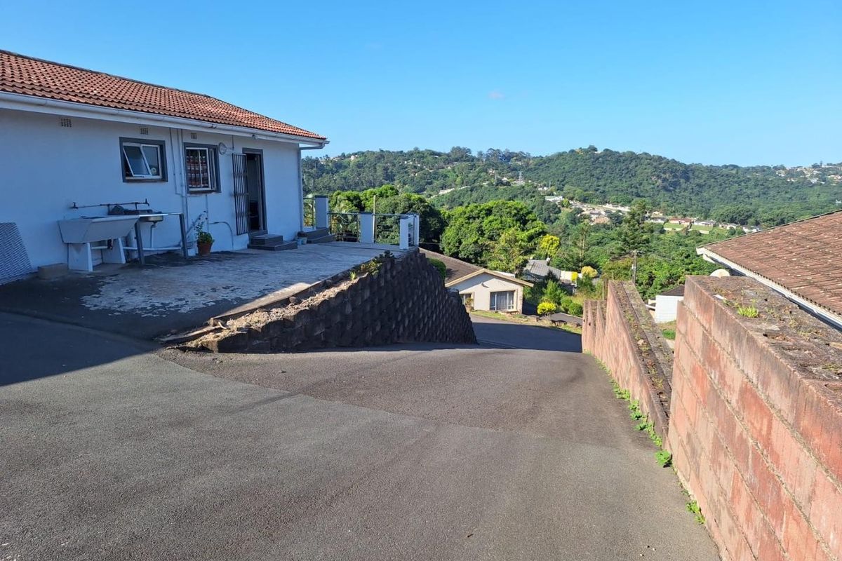Rear exterior view of the townhouse featuring a concrete driveway, retaining wall, and an outdoor laundry area with scenic hillside views.