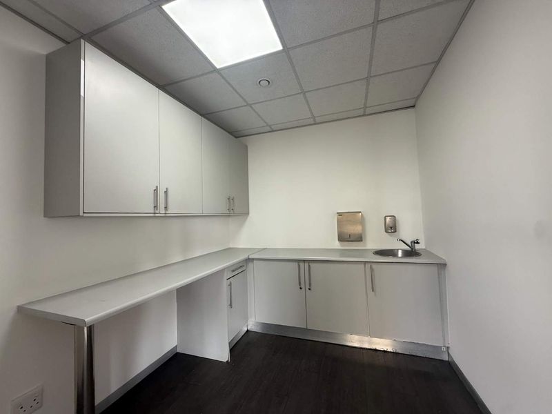 A clean, functional utility or scullery area featuring built-in cabinetry, a stainless steel sink, and a drop ceiling with recessed lighting.