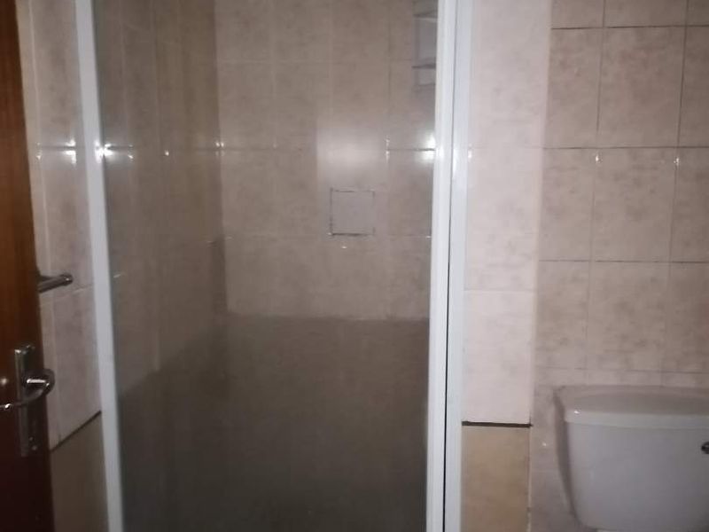 A functional bathroom featuring a shower enclosure with glass door and a standard toilet, finished with neutral ceramic wall and floor tiling.