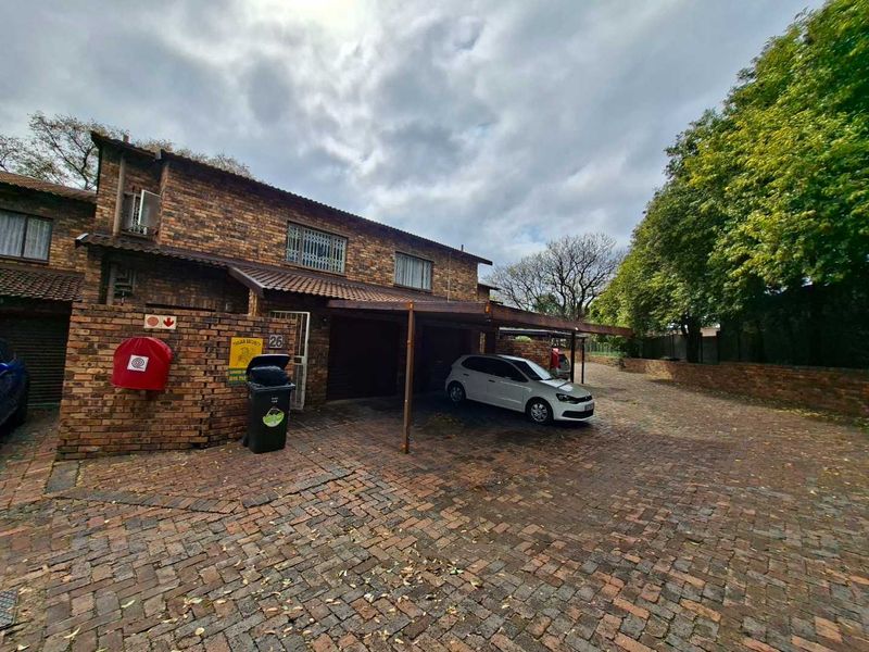Front exterior view of a brick townhouse featuring a paved driveway and a covered carport area.