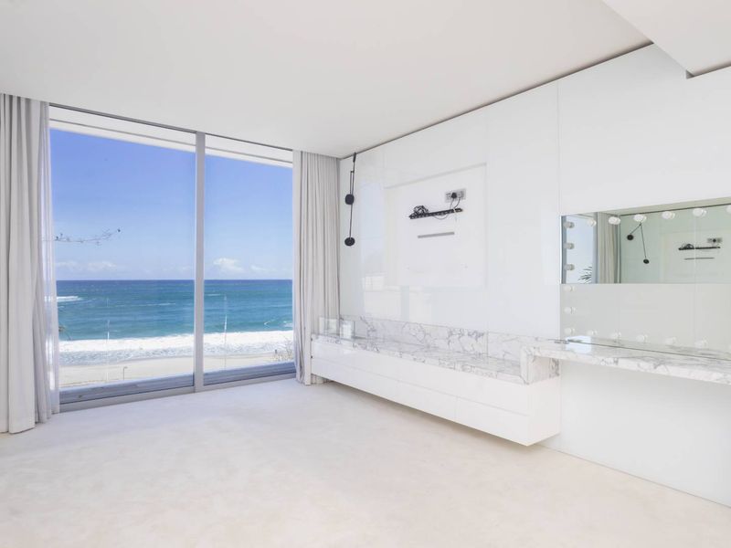 Spacious bedroom featuring floor-to-ceiling windows with panoramic ocean views, sleek built-in cabinetry, and a luxurious marble-topped vanity area.