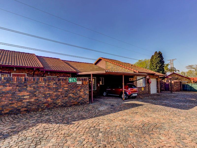 Front exterior view of a cluster home featuring a brick facade, tiled roof, paved driveway, and a covered carport area.