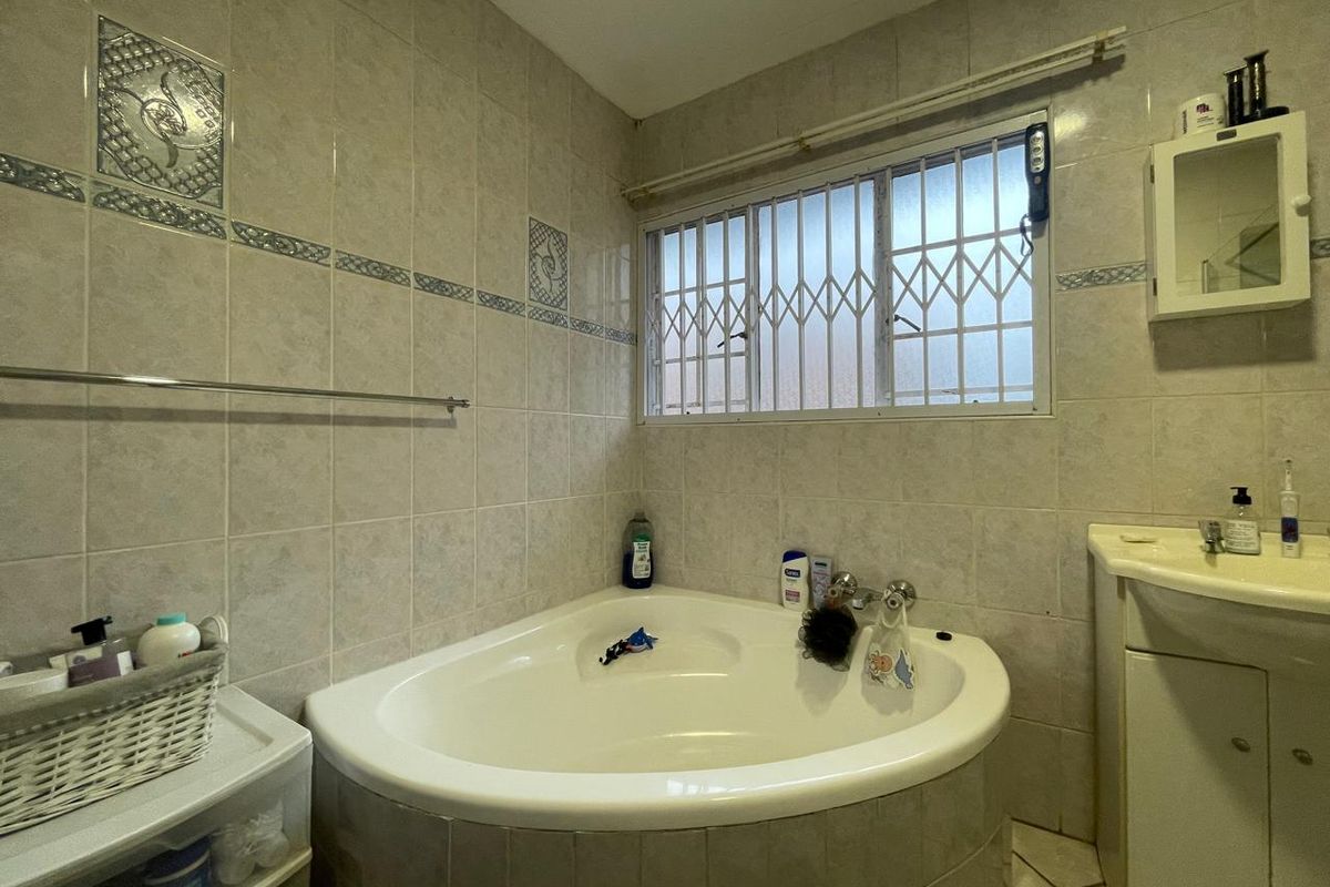 A functional bathroom featuring a corner bathtub, vanity cabinet, and tiled walls, equipped with a security gate on the window.