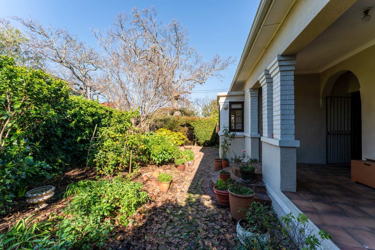 A view of the rear garden area featuring a covered patio, brick paving, and established garden beds alongside the house exterior.