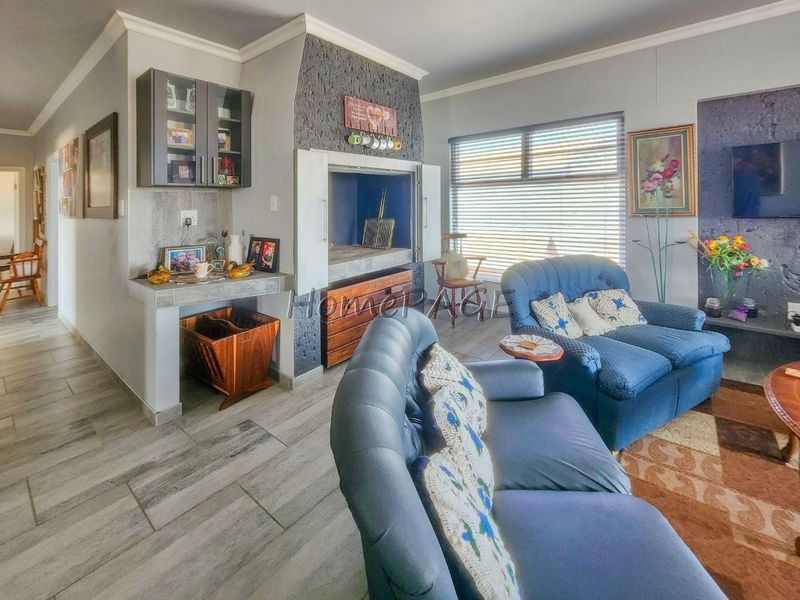 Spacious living room featuring a built-in indoor braai, stone-cladding accent wall, and modern tiled flooring with neutral wall finishes.