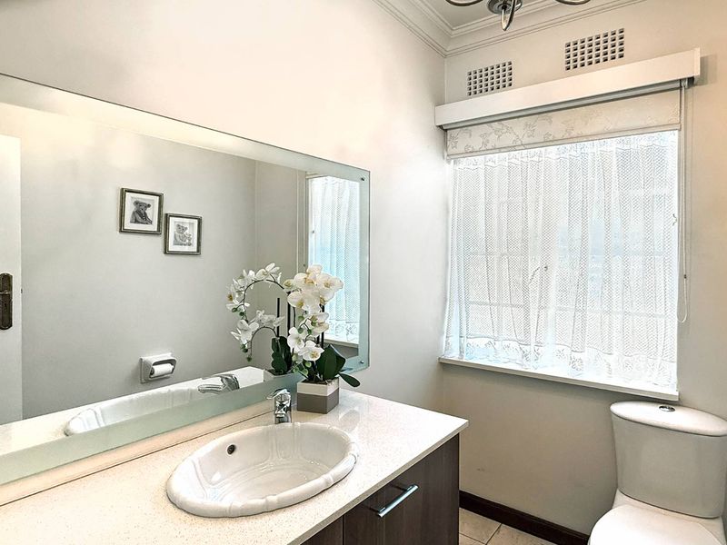 A well-maintained bathroom featuring a vanity with an integrated sink, a large wall mirror, and a toilet, complemented by natural light from the window.