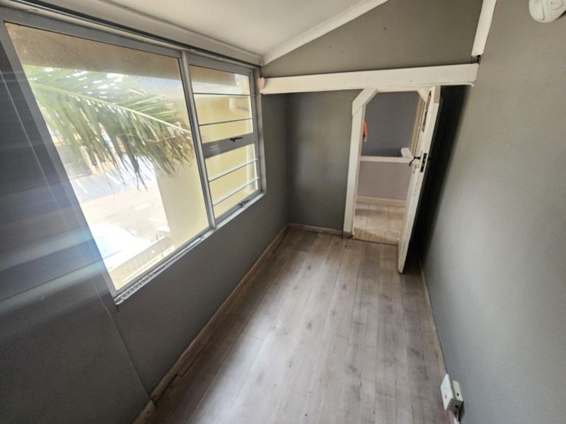 A narrow, empty hallway or transition space featuring laminate flooring, grey walls, and aluminium-framed windows, leading into an adjacent room.