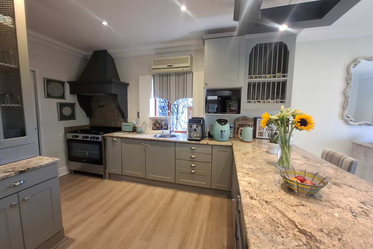 A well-appointed kitchen featuring granite countertops, custom cabinetry, a built-in oven with extractor hood, and a breakfast bar island.