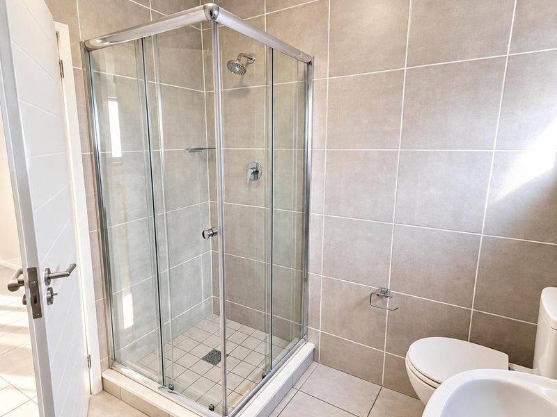 A clean, modern bathroom featuring a corner shower enclosure, tiled walls, a toilet, and a wash basin with neutral finishes.